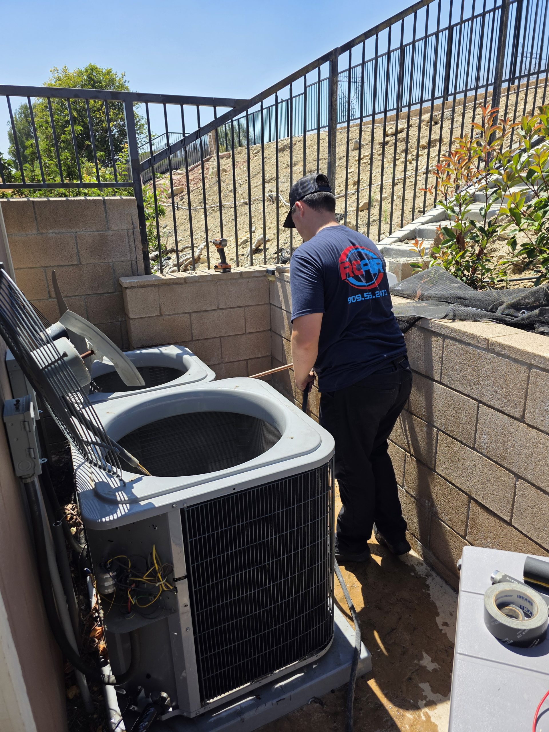 RCAir HVAC tech working on an outdoor AC unit on a warm, blue-sky summer day in Rancho Cucamonga