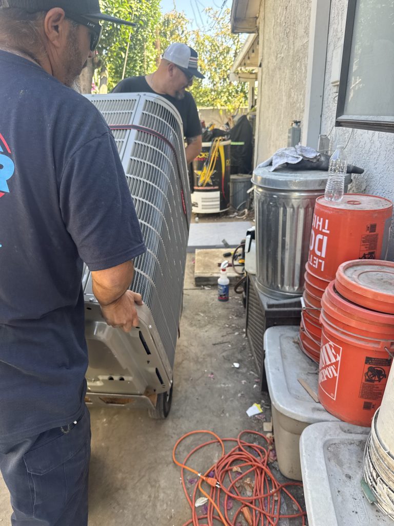 Two RCAir team members rolling in a new outdoor AC unit for installation at a Rancho Cucamonga home.